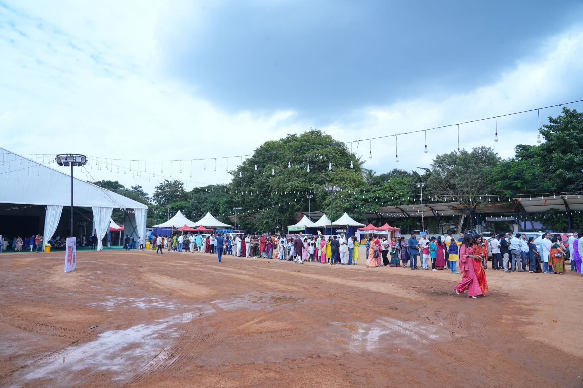 The same line of devotees stretching across the ground towards the stalls, beside the large white tent