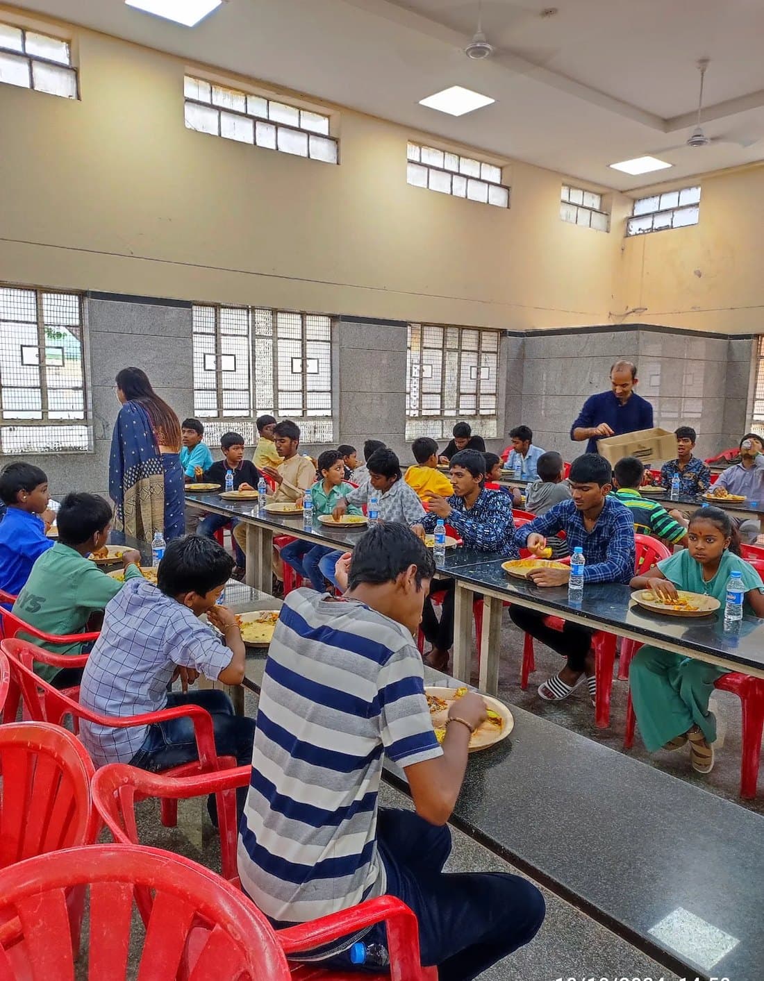 Durgapatra Abhiyan guests seated at long tables in the dining hall, eating bhog from leaf plates